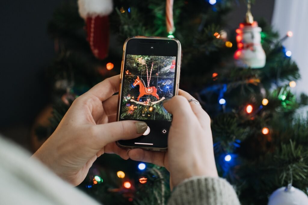 Hands capturing a photo of a red rocking horse ornament on a Christmas tree using a smartphone